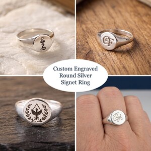 Puede incluir: Un anillo de sello de plata con una cara redonda que presenta varios grabados personalizados, incluyendo una serpiente con un loto, las letras CF, un fénix dentro de una corona de laurel e iniciales en cursiva. El texto Custom Engraved Round Silver Signet Ring es visible.