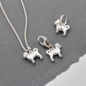 May include: Three silver dog charm pendants, one on a silver chain necklace. The charms are detailed with textured fur and have a realistic dog shape.