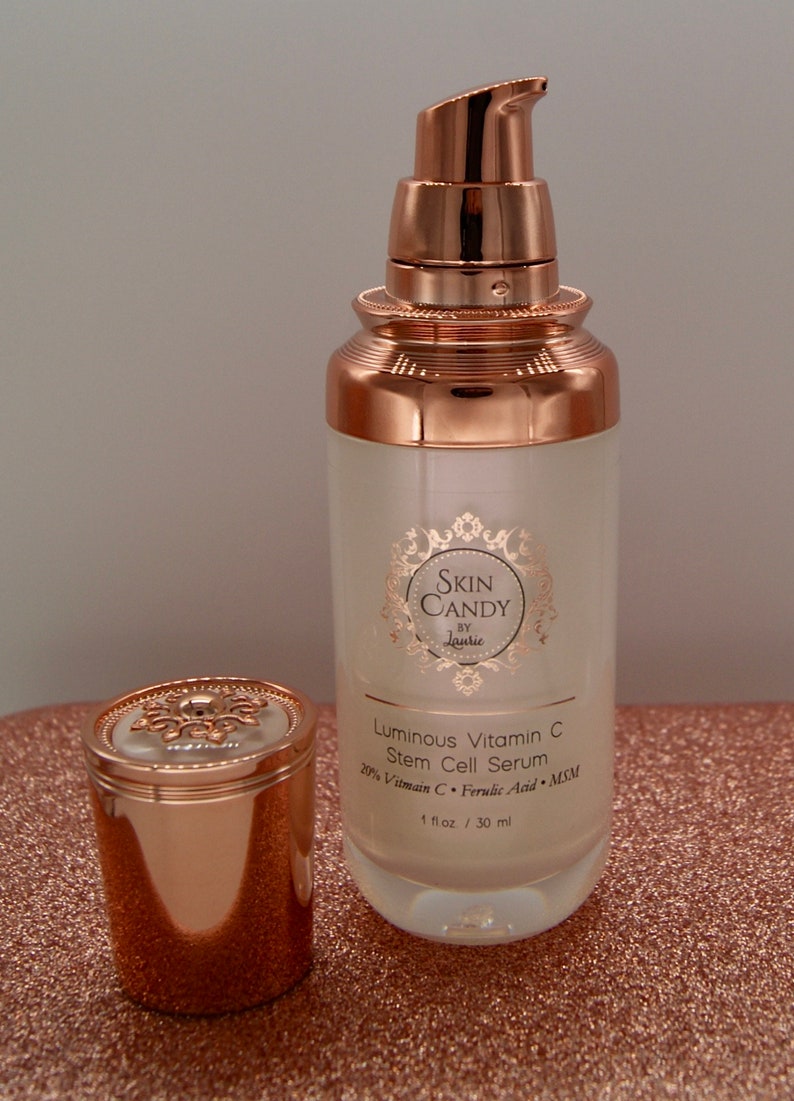 May include: A skincare product bottle with a rose gold pump and cap, next to its cap. The bottle is labeled "Skin Candy" and "Luminous Vitamin C Stem Cell Serum". The bottle contains 1 fl oz / 30 ml of product.