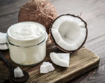 May include: A glass jar filled with white coconut yogurt, with two halves of a coconut and coconut pieces on a wooden cutting board.