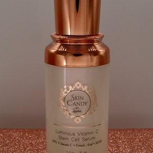 May include: A skincare product bottle with a copper-colored cap and base. The bottle is labeled "Skin Candy by Laurie" and contains "Luminous Vitamin C Stem Cell Serum." The bottle is 1 fl oz / 30 ml.
