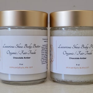 May include: Two glass jars with gold lids containing body care products. The jar on the left contains shea butter and the jar on the right contains shea body polish. Both jars are labeled "Luxurious Shea Body Butter/Polish Organic/Fair Trade Chocolate Amber 8 oz skincandybylaurie.com"