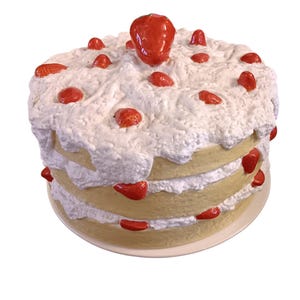 May include: A three-layered cake with white frosting and red strawberry accents. The cake sits on a round, off-white plate. The top of the cake is decorated with a large strawberry and several smaller ones.