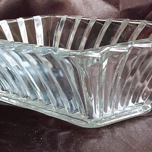 May include: A clear glass bowl with a geometric design. The bowl has a square base and a starburst pattern on the sides.
