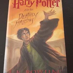 Puede incluir: Portada del libro "Harry Potter y las Reliquias de la Muerte" de J.K. Rowling. La ilustración muestra a Harry Potter con el brazo extendido sobre un fondo naranja y amarillo. El título es rojo.
