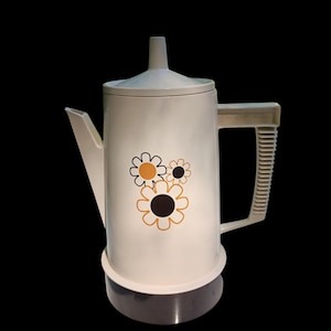 Puede incluir: Cafetera eléctrica blanca con un diseño floral en naranja y negro. La cafetera tiene un pico, asa y tapa. La base es de color gris oscuro. La manija tiene la palabra "REGAL" impresa.