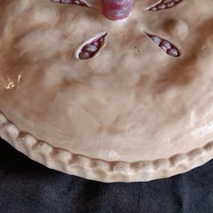 Könnte beinhalten: Eine Keramik-Tortenform mit brauner Glasur und einem gewellten Rand. Die Tortenform ist mit roten und weißen Kirschen verziert.