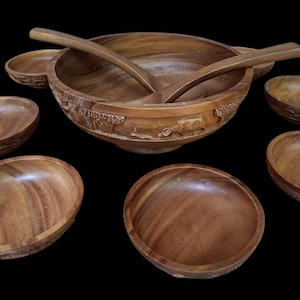 Könnte beinhalten: Ein Set aus Holzsalatschüsseln und Servierlöffeln. Die große Schüssel hat ein geschnitztes Design und die kleineren Schüsseln sind schlicht. Das Set ist aus Naturholz gefertigt und hat eine warme braune Farbe.