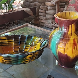 Pode incluir: Um jarro de cerâmica amarelo, verde e castanho com uma pega e uma tigela de cerâmica a condizer amarelo, verde e castanho. A tigela tem uma borda ondulada.