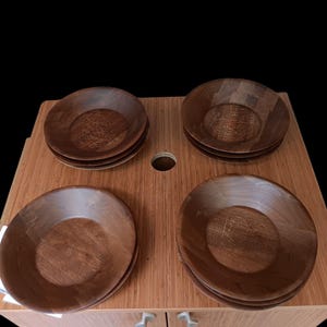 May include: Four wooden bowls with a rich brown finish are stacked on a wooden surface. The bowls have a simple, classic design, with a slightly curved rim and a smooth interior. The bowls are arranged in two stacks of two.