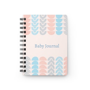 Puede incluir: Un diario de espiral rosa y azul con un patrón geométrico y el texto "Baby Journal" en la portada.