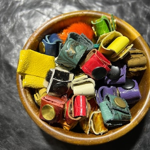 May include: A wooden bowl filled with colorful leather finger rings. The rings are made of different colors and patterns, including black and white zebra print, red, yellow, green, and blue.