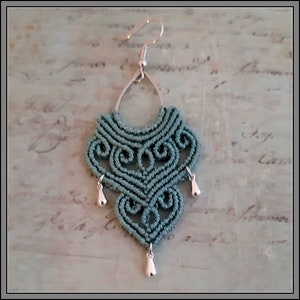 May include: Teal blue macrame earrings with silver teardrop accents. The earrings are made with a knotted rope design and have a silver hook closure.