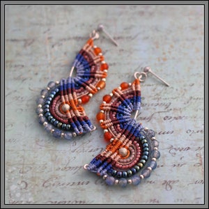 May include: Handmade macrame earrings in a fan shape, featuring a combination of blue, orange, and brown threads. The earrings are adorned with small beads in shades of blue and orange, and have silver-colored ear wires.