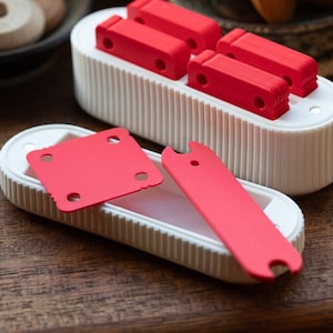 May include: Two white plastic containers with red plastic pieces inside. The containers have a ribbed texture. The red pieces are various shapes, including squares and rectangles.
