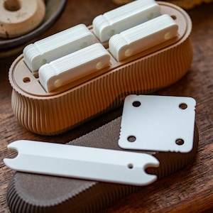 May include: A brown plastic container with multiple compartments filled with white plastic pieces. The container has a textured surface. There are two additional white plastic pieces on a brown surface.