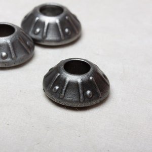 Op de afbeelding: Drie zilveren metalen decoratieve doppen met een reli&euml;fdesign. De doppen zijn rond van vorm met een gat in het midden.