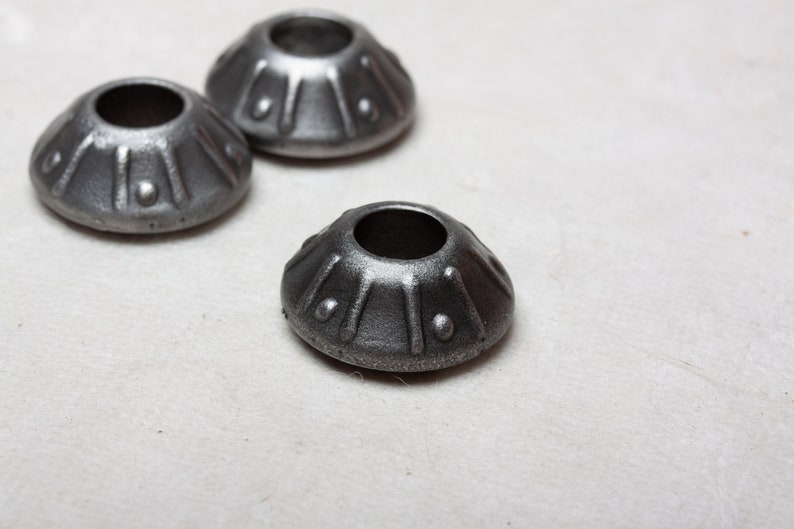 Op de afbeelding: Drie zilveren metalen decoratieve doppen met een reli&euml;fdesign. De doppen zijn rond van vorm met een gat in het midden.