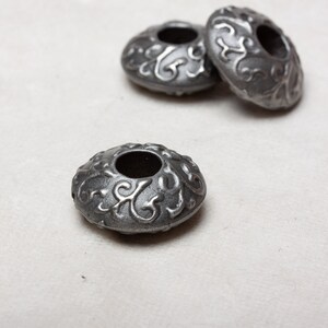 Puede incluir: Tres cuentas de metal plateado con un dise&ntilde;o floral decorativo. Las cuentas tienen un agujero en el centro y est&aacute;n dise&ntilde;adas para la elaboraci&oacute;n de joyas.