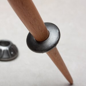 Op de afbeelding: Een houten tripodpoot met een metalen ring en twee metalen voeten. De ring is donkergrijs en de voeten zijn lichtgrijs.