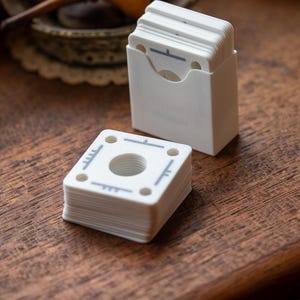 May include: A stack of white plastic discs with a grey design and a hole in the centre. The discs are stacked on a wooden surface.
