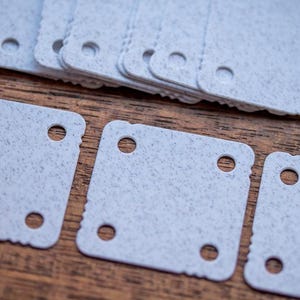 May include: Four white square plastic tiles with rounded corners and four holes each. The tiles have a speckled texture.