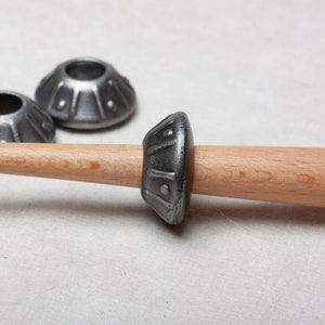 Op de afbeelding: Een houten spil met een metalen spoel, twee extra metalen spoelen zijn zichtbaar op de achtergrond.