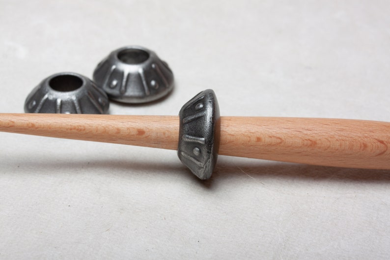Op de afbeelding: Een houten spil met een metalen spoel, twee extra metalen spoelen zijn zichtbaar op de achtergrond.