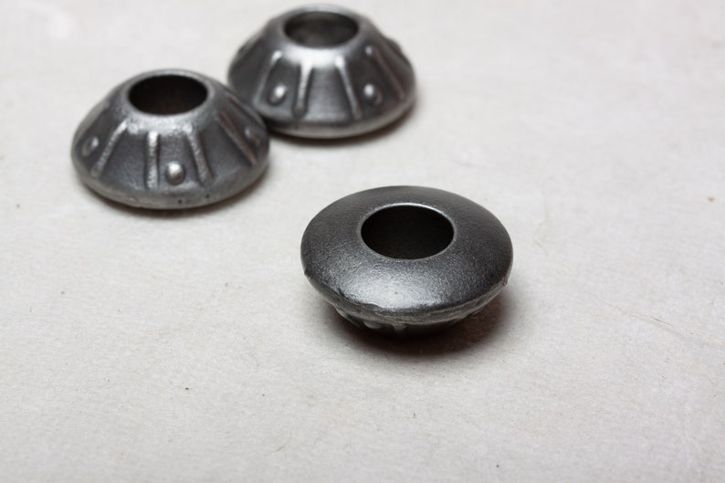 Op de afbeelding: Drie zilveren metalen meubellegdoppen met een decoratief ontwerp. De doppen hebben een ronde bovenkant met een gat in het midden en een geribbelde basis.