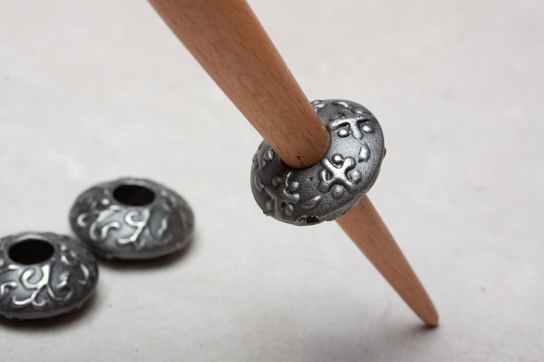 Puede incluir: Un huso de hilar de madera con tres hileras de metal plateado. Las hileras tienen un dise&ntilde;o decorativo.