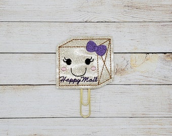 May include: A gold glitter paperclip with a happy mail design. The paperclip has a purple bow and a smiling face. The text "Happy Mail" is written on the paperclip.