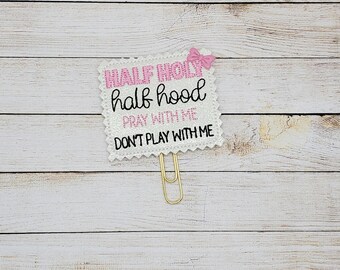 May include: A white and pink glitter paperclip with the text "Half holy half hood pray with me don't play with me".
