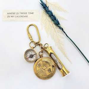 May include: A gold-toned keychain featuring a compass, an hourglass, and a circular calendar. The keychain has a small tag with the quote "Where is there time in my calendar?"
