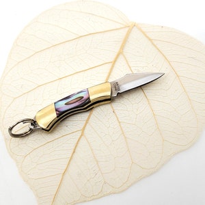May include: A small, gold-colored pocket knife with a mother-of-pearl handle and a silver blade. The knife has a key ring attached to it.