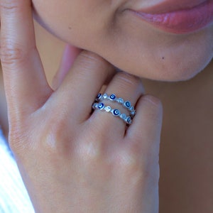 May include: A silver ring with a double row of blue evil eye charms and clear cubic zirconia stones.