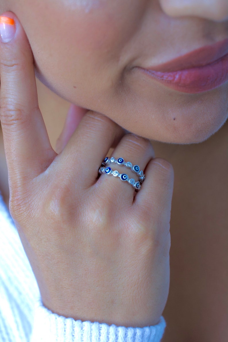 May include: A silver ring with a double row of blue evil eye charms and clear cubic zirconia stones.
