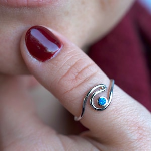 May include: A silver ring with a blue opal stone set in a wave design. The ring is worn on the thumb.
