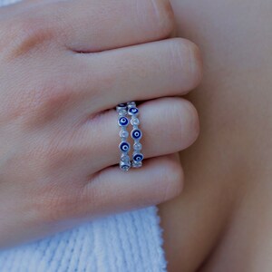 May include: A silver ring with a double row of blue evil eye charms. Each charm has a white center and is surrounded by small clear stones.