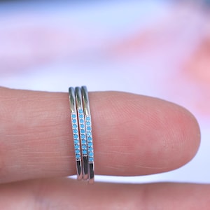 Op de afbeelding: Drie dunne zilveren ringen met een rij lichtblauwe stenen op elke ring.