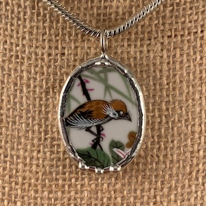 May include: A silver chain necklace with an oval pendant featuring a vintage china bird illustration. The bird is brown and white with green and pink floral details.
