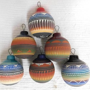May include: Six hand-painted ceramic ornaments with a Southwestern design. Each ornament is a different color, including blue, orange, and black, with geometric patterns and a loop for hanging. The ornaments are arranged in a pyramid shape.