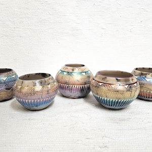 May include: Five small, round ceramic bowls with a decorative, etched design. The bowls feature a color gradient of blues, purples, and browns. Each bowl has a unique pattern, adding to their handcrafted appeal.