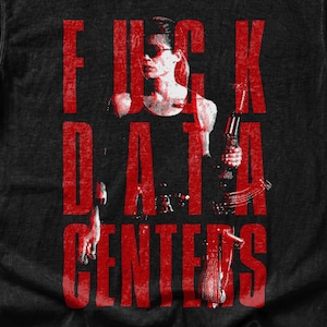 May include: A black short-sleeve t-shirt featuring a distressed red graphic print of a person holding a firearm. The text FUCK DATA CENTERS is printed in large, bold red letters over the central figure. The shirt has a crew neck and a tag.
