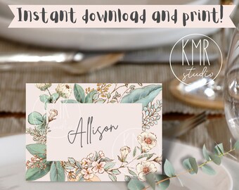 May include: A printable place card with a floral design featuring green leaves, white flowers, and a light pink background. The name "Allison" is written in black cursive script on a white rectangle.