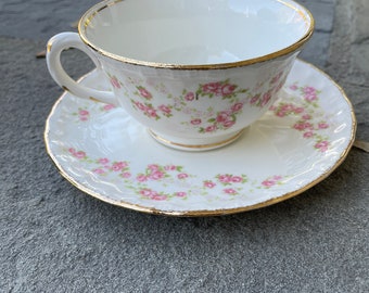 May include: A white teacup and saucer set with a pink and green floral pattern and gold trim.