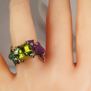 May include: A gold ring with a large green oval gemstone surrounded by smaller green and purple gemstones.