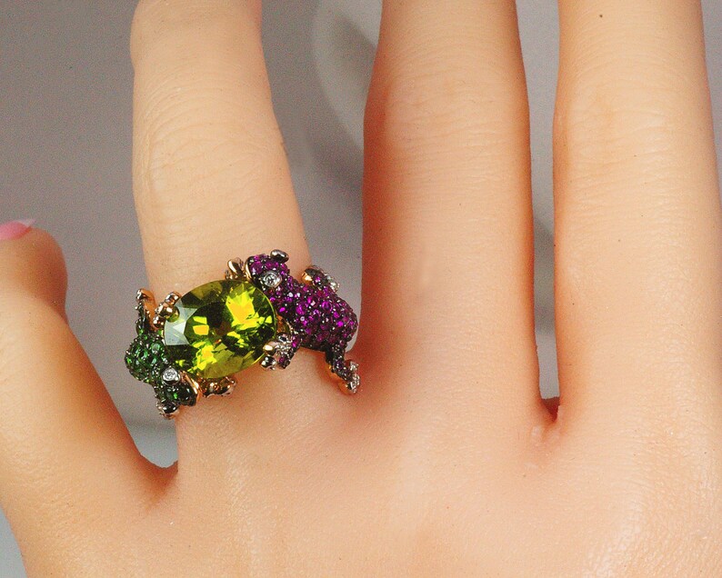 May include: A gold ring with a large green oval gemstone surrounded by smaller green and purple gemstones.