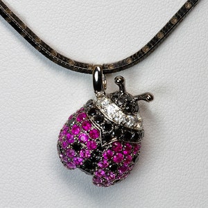 May include: A black and pink jeweled ladybug pendant necklace with a black chain. The ladybug is made of metal and has a black and white diamond band around its middle.