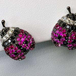 May include: A pair of black metal ladybug earrings with pink and black gemstones. The earrings are set with small round stones.