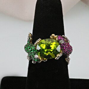 May include: A gold ring with a large green gemstone surrounded by smaller green, pink, and white gemstones.
